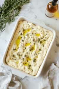 This image shows the dough being pressed into a baking dish and topped with olive oil and Italian seasoning.