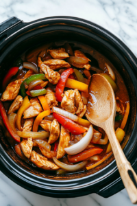 A pair of tongs or a fork is used to shred the cooked chicken and mix it with the flavorful sauce in the slow cooker.