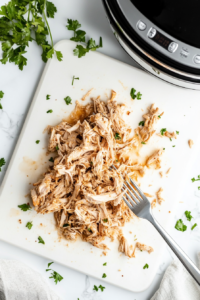 Two forks are used to shred the tender, cooked chicken breasts into bite-sized pieces.