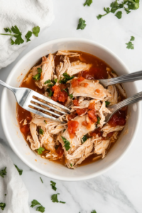 Two forks being used to shred tender chicken breasts into smaller pieces, creating a juicy and flavorful base for the keto dish.