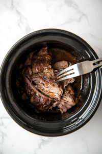 This image shows tender pork being shredded with two forks, breaking it into small, flavorful pieces for serving.