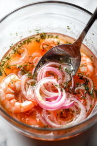 This image shows freshly cooked shrimp being transferred to a jar of pickling liquid, where they will absorb the flavors of the herbs and spices.