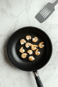 This image shows shrimp cooking in a hot skillet, turning golden and juicy, ready to be added to the salad.