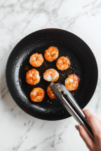 this image shows Close-up of shrimp in a skillet, reaching the perfect golden brown color for keto coconut shrimp.