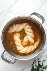 This image shows the shaped dough simmering in a pot of seasoned broth to infuse it with a rich, savory flavor.