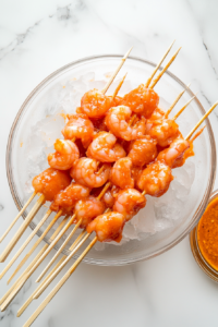 Marinated shrimp being threaded onto bamboo skewers, prepared for grilling.