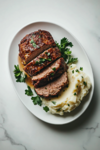 This image shows slices of crockpot meatloaf served on a plate, paired with a side of mashed potatoes and garnished with fresh cilantro for a complete meal.