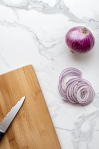 This image shows a red onion being sliced into thin rings, preparing it to be mixed with cucumbers for a flavorful cucumber salad.