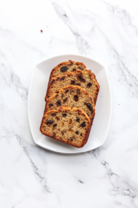 This image shows the Jamaican banana bread being sliced with a knife and served, showcasing the moist interior with pecans and raisins visible.