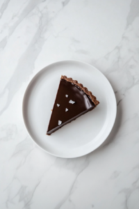 This image shows the vegan dark chocolate tart sliced and ready to serve, with its glossy chocolate filling and crisp crust creating a delectable dessert presentation.