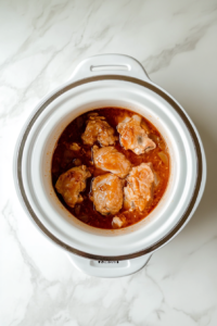 This image shows a slow cooker lid in place, with the appliance set to cook the chicken thighs slowly to tender perfection, infusing them with the sauce's rich flavors.