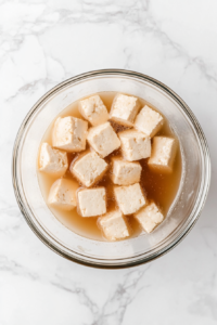 This image shows tofu nuggets being soaked in a flavorful broth to absorb spices and enhance their taste for Wendy's-style spicy chicken nuggets.