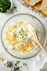 hand using a spatula to spread a creamy mixture of shredded mozzarella, mayonnaise, sour cream, and green onions over the bread.