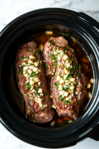 This image shows minced garlic being evenly spread over the pork tenderloin in the slow cooker, enhancing the dish with its aromatic flavor.