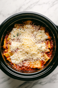 This image shows the creamy ricotta mixture being spread over lasagna noodles, followed by a generous sprinkle of shredded cheese for a rich layer.