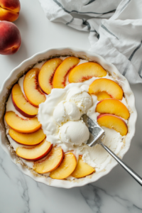 This image shows softened vanilla ice cream being spread smoothly over the layer of cinnamon-coated peaches, forming the top creamy layer of the peach cream pie