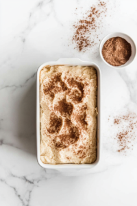 This image shows the final layer of cinnamon-sugar being generously sprinkled on top of the bread batter, adding a sweet and flavorful crust to the baked loaf.