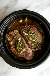 This image shows black pepper being sprinkled over the pork tenderloin, adding a touch of spice and enhancing the savory flavors in the slow cooker.