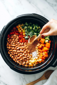 This image shows a variety of spices, including chili powder and cumin, being sprinkled over the slow cooker mixture to enhance the chili’s bold flavor.