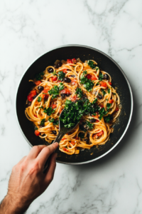 this image shows Fresh parsley and cracked black pepper being sprinkled over the pasta in the pan, enhancing the aroma and taste of the Vegan Green Olive Pasta Sauce.