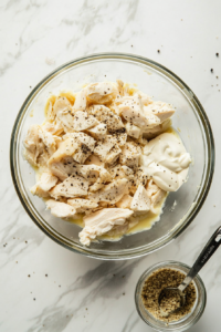 This image shows an assortment of seasonings being sprinkled over the shredded chicken and mayo mixture, adding flavor to the protein-packed carnivore chicken salad.