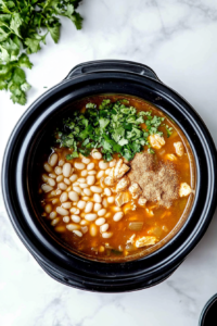 This image shows all the ingredients for Crockpot White Chicken Chili being stirred together in the slow cooker, ensuring they are evenly combined before cooking.