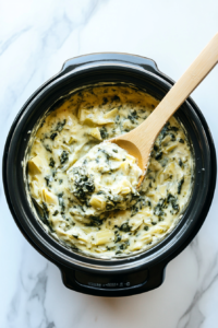 This image shows the creamy spinach artichoke dip being stirred thoroughly inside the slow cooker to ensure an even, smooth consistency before serving.