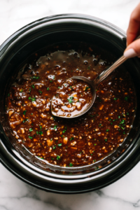 This image shows a spoon stirring the remaining sauce in the crockpot to thicken it and prepare it for drizzling over the cooked chicken.