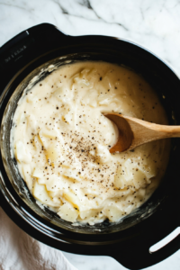 This image shows a stirring spoon mixing the hashbrowns and other soup ingredients in the crockpot to ensure even cooking and flavor blending.