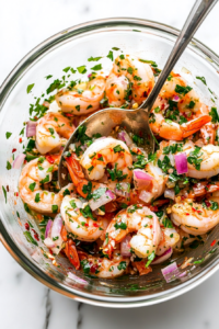 This image shows the pickled shrimp being stirred in a jar to evenly distribute the fresh herbs and flavors before plating.