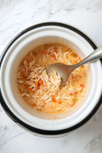 This image shows a spoon stirring the shredded chicken, creamy gravy, and cooked vegetables together in the crockpot, ensuring the filling is well-mixed and flavorful.