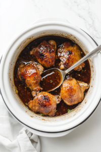 This image shows a spoon stirring the rich sauce of soy sauce, ketchup, honey, garlic, and basil in a slow cooker, coating the tender chicken thighs evenly for maximum flavor.