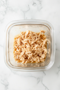 This image shows shredded vegan chicken being placed in an airtight container for storage, ready to use in recipes.