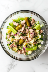 this image shows spoon being used to taste the tuna salad, ensuring the seasoning is perfectly balanced before serving.