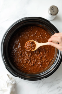 This image shows a spoonful of chili being tasted to check the seasoning, ensuring the flavors are balanced and ready for serving.