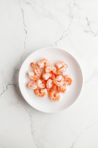 This image shows frozen shrimp being thawed in a bowl of water, the first step in preparing the shrimp cucumber bites appetizer.