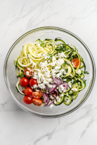 This image shows a bowl of Greek zucchini salad topped with crumbled feta cheese, adding a creamy and tangy flavor to the dish.