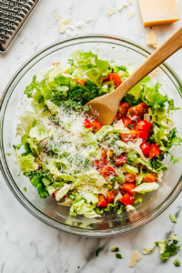 this image shows bowl of fresh Romaine lettuce, juicy diced Roma tomatoes, and shredded Parmesan cheese being tossed together to create a vibrant base for the Keto Cajun Caesar Salad.