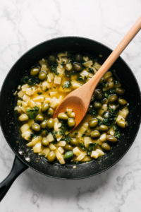 this image shows Cooked pasta being tossed in a pan with the flavorful olive and garlic sauce, combining all the ingredients for the Vegan Green Olive Pasta Sauce.