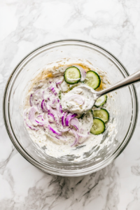 This image shows the ingredients being tossed together, ensuring the cucumbers and onions are evenly coated with the creamy dressing.