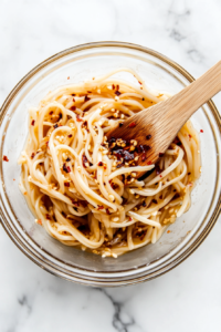 This image shows the cooked noodles being thoroughly tossed in the creamy garlic sauce, ensuring every strand is evenly coated with the rich and flavorful mixture.