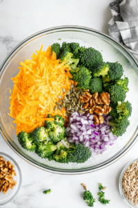 This image shows chopped onions, walnuts, and sunflower seeds being added to the broccoli and cheese mixture in a bowl, enhancing the texture and flavor.