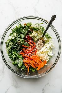 This image shows the cabbage, carrots, and ramen noodles being tossed with the prepared dressing, then garnished with golden toasted sesame seeds for a final touch.