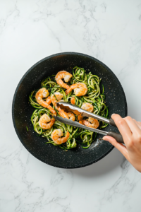 This image depicts shrimp being mixed into the zucchini noodles in the pan, ensuring the flavors combine evenly.