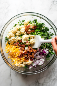 This image shows the pea salad being carefully tossed with a spoon until the creamy dressing evenly coats all the peas and mix-ins for a flavorful result.