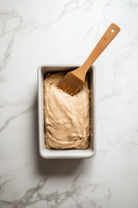 This image shows the bread batter being evenly spread into a greased loaf pan, ready to be baked in the oven.