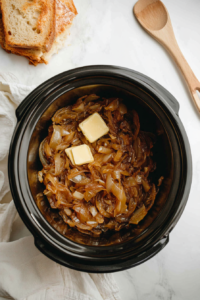 This image shows a top-down shot of the caramelized onions being transferred into the slow cooker, preparing for the next stage of the soup.