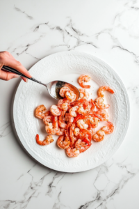 this image shows Freshly cooked Old Bay shrimp being plated onto a white serving dish.