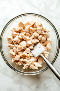 This image shows the drained shredded chicken being transferred from the can into a clean white mixing bowl to begin assembling the carnivore chicken salad.