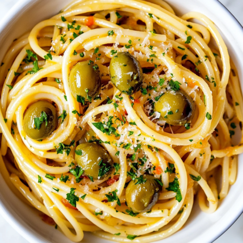 this image shows A delectable plate of Vegan Green Olive Pasta Sauce served on a white plate, garnished with shredded cheese, chopped cilantro, and sliced green olives, creating a creamy and flavorful dish.